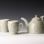 A green tinted white teapot with two matching teacups