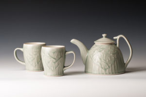A green tinted white teapot with two matching teacups