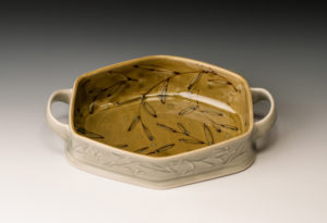 A white hexagonal plate with two handles and a yellow interior with thin painted leaf outlines throughout the piece. Created by Lana Heckendorn