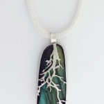 Pendant of silver tree branches crawling down the front of a deep green semiprecious stone. Created by Janet Kofoed