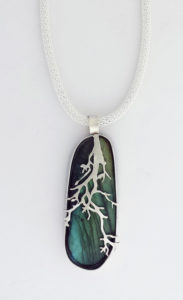 Pendant of silver tree branches crawling down the front of a deep green semiprecious stone. Created by Janet Kofoed