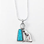 A pendant of a silver cat and a brilliant blue semi-precious stone laid in silver. Created by Janet Kofoed