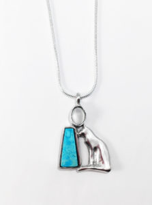 A pendant of a silver cat and a brilliant blue semi-precious stone laid in silver. Created by Janet Kofoed