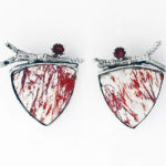 Reuleaux triangle shaped earrings by Janet Kofoed, each stark white with spatters of red, a silver branch, and semiprecious stone at the top