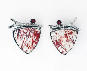 Reuleaux triangle shaped earrings by Janet Kofoed, each stark white with spatters of red, a silver branch, and semiprecious stone at the top