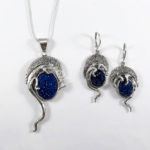 A pendant by Janet Kofoed depicting a silver animal cradling a shining oval cerulean colored stone