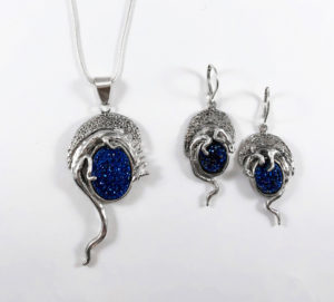 A pendant by Janet Kofoed depicting a silver animal cradling a shining oval cerulean colored stone