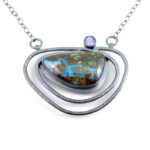 Silver pendant by Yanina Siani with three concentric ovals holding a blue and brown stone and a faceted gemstone.