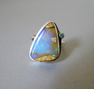 Silver ring by Yanina Siani holding a small faceted gemstone and a larger smooth triangle blue opalescent stone