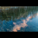 Closeup photograph by Andy Smith of clear rippling water reflecting pink clouds.