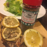 A shaker of Country Herbs Tuscan Bread Dip Seasoning behind meat and lemons sprinkled with the seasoning