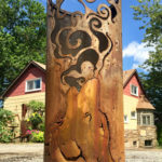 A cylindrical metal garden sculpture with a wolf howling a smoke pattern cut into the sides. Created by Sandra Webberking.