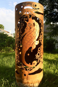 A cylindrical metal garden sculpture with a seahorse surrounded by bubbles cut into the sides. Created by Sandra Webberking.