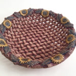 A ceramic piece in the style of a realistic deep brown basket with flower decorations created by Susan Wechsler