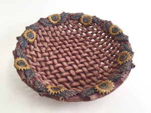 A ceramic piece in the style of a realistic deep brown basket with flower decorations created by Susan Wechsler