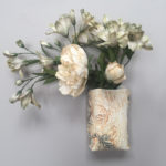 A ceramic off white wall flower pot with a bouquet of white flowers inside of it. Created by Susan Wechsler.