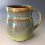 An ochre mug with a small teal band by Deborah Williams