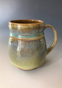 An ochre mug with a small teal band by Deborah Williams