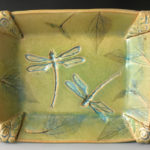 A yellow green plate created by Deborah Williams depicting two dragonflies and several leaves