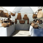 A collection of Samuel Yao’s hand woven palm baskets in a booth setting. The white background boosts the rich colors of each basket.