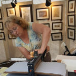 Maryann Cannon in her booth shows the process of transferring her inked metal etchings onto cotton paper.