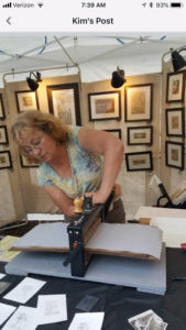 Maryann Cannon in her booth shows the process of transferring her inked metal etchings onto cotton paper.