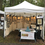 A collection of Maryann Cannon's work in a booth setting. Her pieces on the walls are illuminated in warm yellow light.