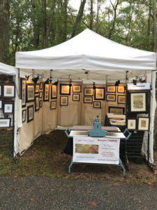 A collection of Maryann Cannon's work in a booth setting. Her pieces on the walls are illuminated in warm yellow light.