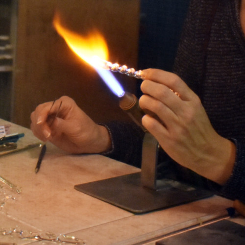 hands flameworking with a clear glass rod and torch