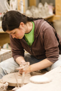 Tessa pressing a clay molding pot on a potters wheel