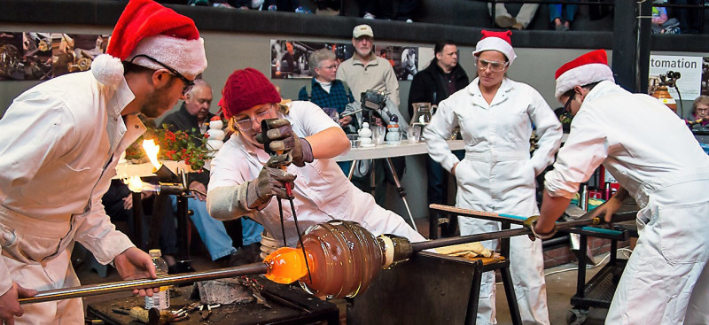 Big Glass Blast team creating a giant glass object, dressed in white suits and Santa hats