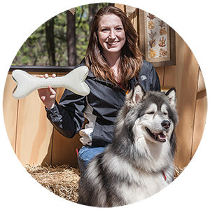 Woman sitting on straw, holding a large glass bone with her dog during PAWS for art.