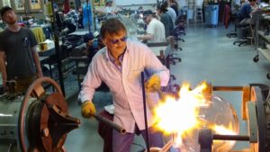 Dennis Briening shaping glass with crowd of working artists behind him.