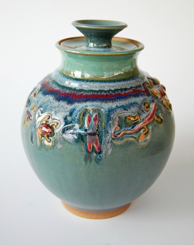 Teal covered pot with small creatures carved and painted around the body. Created by Marsha Dowshen
