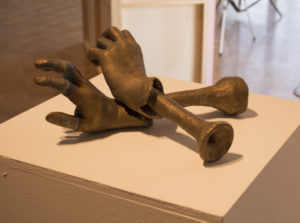 Bronze color bones connecting at the wrist to two fleshy hands that are reaching and grabbing. Created by Amy Rubinstein.