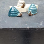 Three clay snails. One has a dark blue shell, the next light blue, and a third snail with its white shell. Created by Tessa Carlton.
