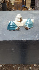 Three clay snails. One has a dark blue shell, the next light blue, and a third snail with its white shell. Created by Tessa Carlton.