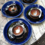 Matching bowls deep green rims and burnt orange insides sit on four matching platters with dark green wells. Created by Tessa Carlton.