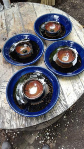 Matching bowls deep green rims and burnt orange insides sit on four matching platters with dark green wells. Created by Tessa Carlton.