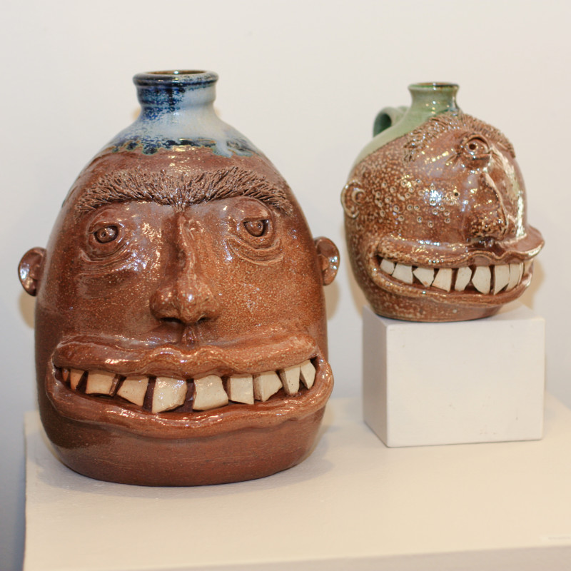 Two head-shaped jugs with colored tops and large, toothy smiles. Created by Phyllis Seidner