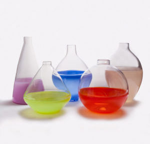 Five glass containers with the bottom halves painted purple, yellow, blue, red, and tan by Skitch Manion