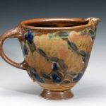 A wide pitcher with a peach colored flower motif around the body by Terry Plasket