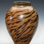 A tall vase by Terry Plasket with stripes winding down the brown body