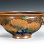 A wide serving bowl with a peach colored flower motif around the body by Terry Plasket