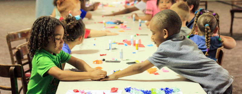 Group of young children at a long table creating butterflies with tissue paper.