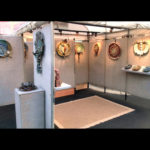 John Cheer's 10x10 booth display.. Cheer's work is displayed on the walls, each highlighted with a warm yellow light.