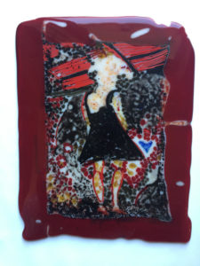 A fused glass depiction of a woman in a black dress with a black background and a maroon frame