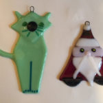 Two fused glass ornaments by Deborah DiMarco, one of a green cat and the other of Santa Claus