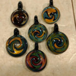 six glass pendants with swirling orange, green, and blue colors by Bill Futer