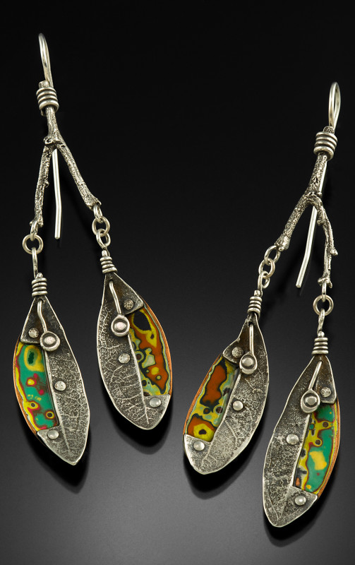 Each silver earring is shaped like a twig with two leaves, decorated with rivets and markings. Created by Logan Louis.